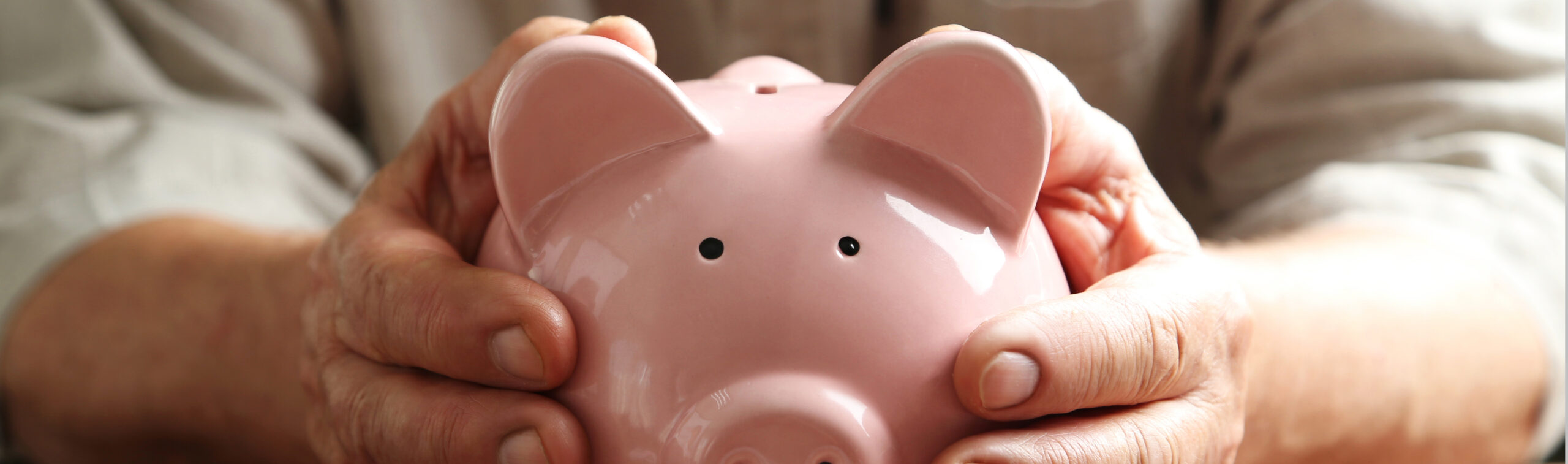Hands,of,old,senior,with,piggybank,on,a,wooden,table